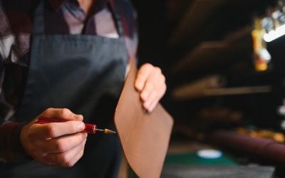 Young focused experienced master craftsman makes leather goods at his workplace