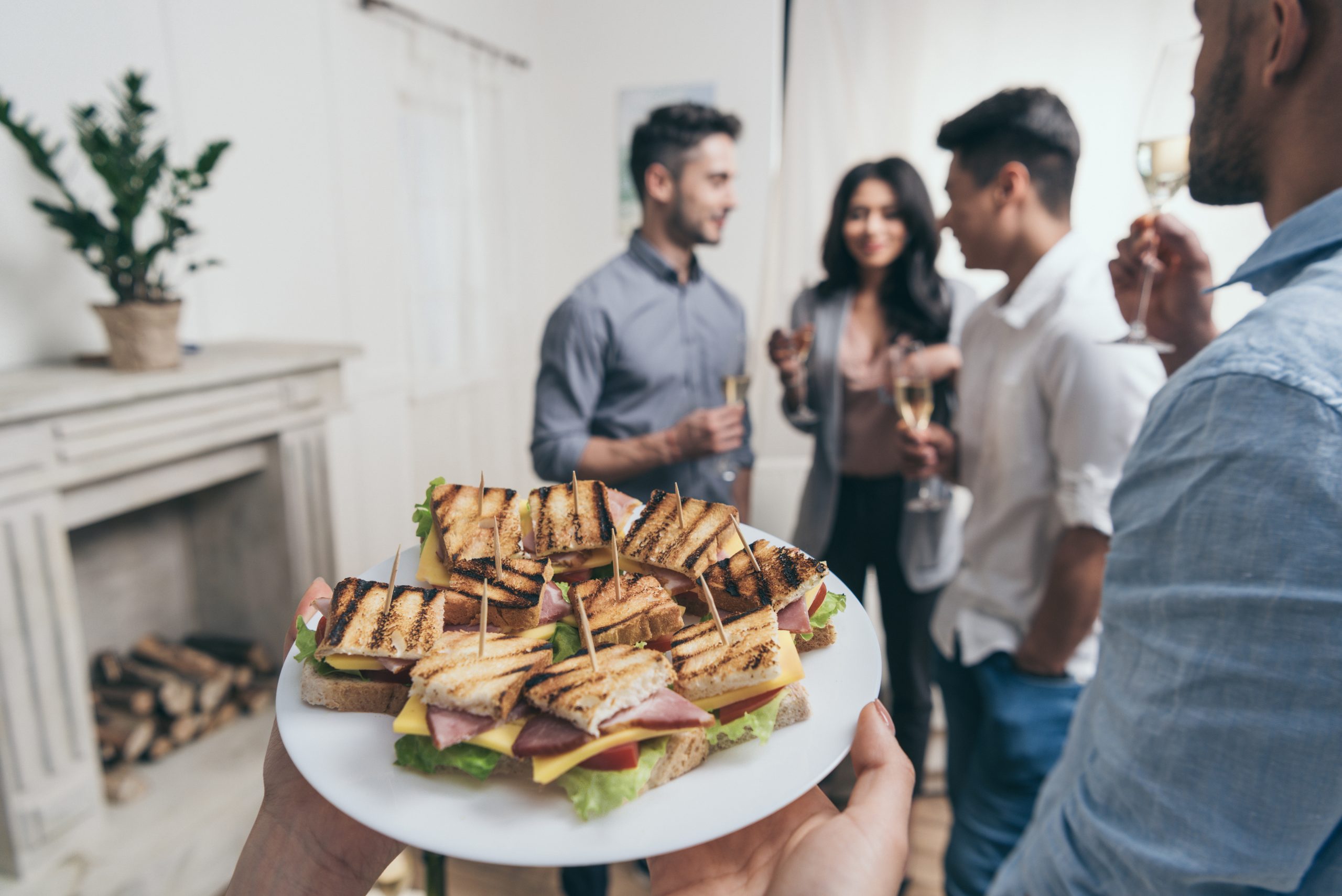 person holding plate with tasty sandwiches while smiling young friends drinking