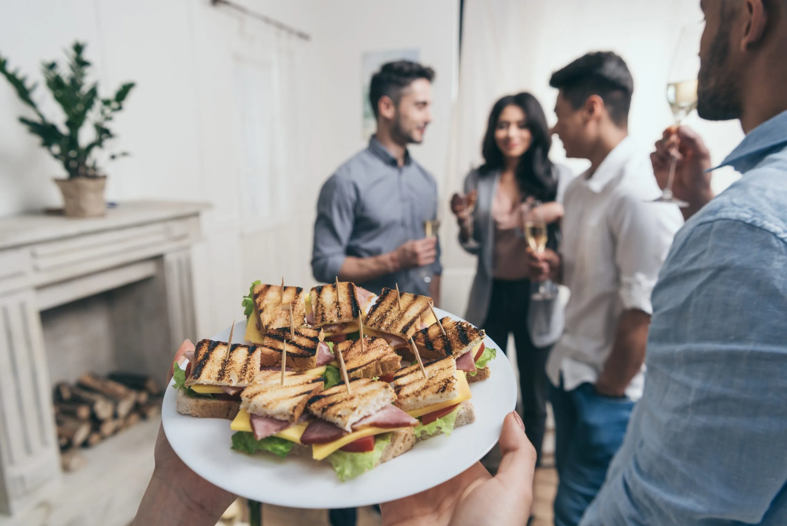 person holding plate with tasty sandwiches while smiling young friends drinking